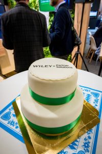 A two-layer round cake, iced in white with green ribbons. Across the top it reads "Wiley Partner Solutions"